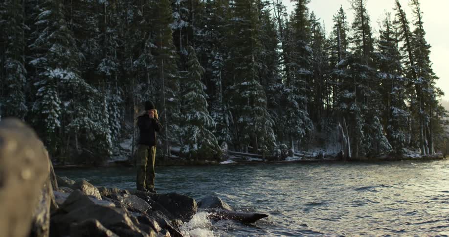 A woman is standing on rocks by the water
