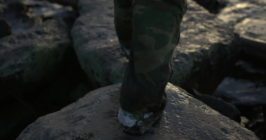 A person walks on a rocky area near some water