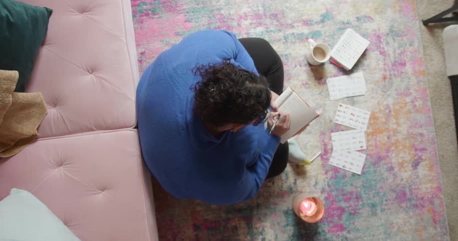A woman sitting on an area rug leaning against the sofa journaling
