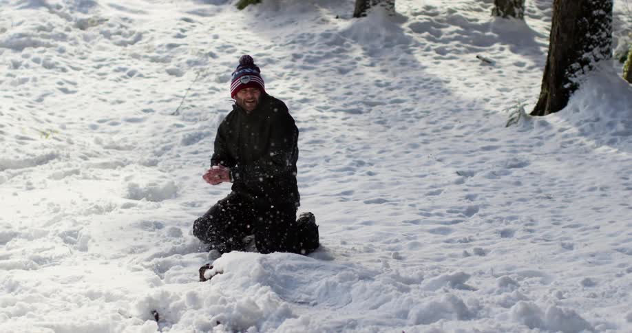 A man on his knees is throwing snowballs