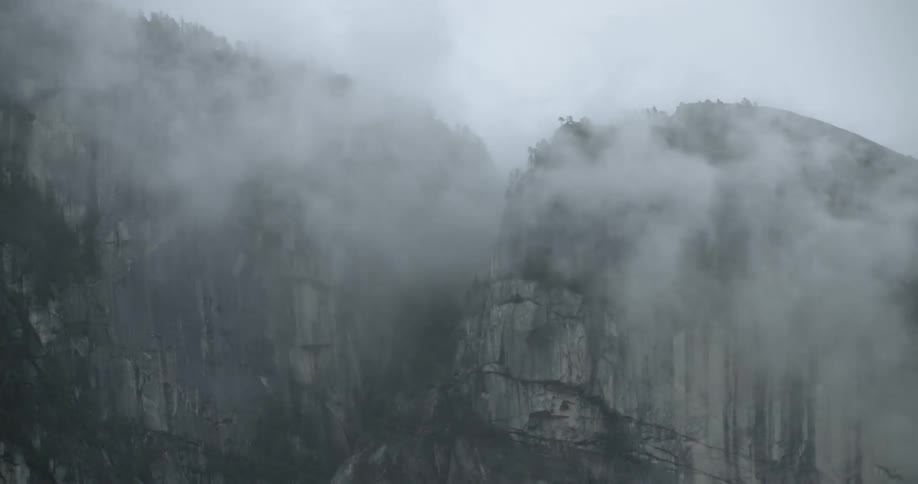 Clouds and fog move past and over a straight cliff mountain ridge