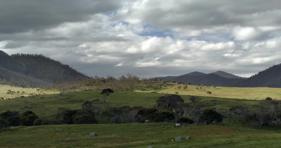 The sun peeks through storm clouds and shines on rolling hills