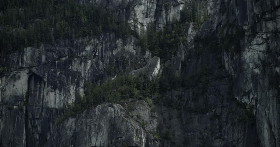 Smoke moves next to a steep forest covered cliff