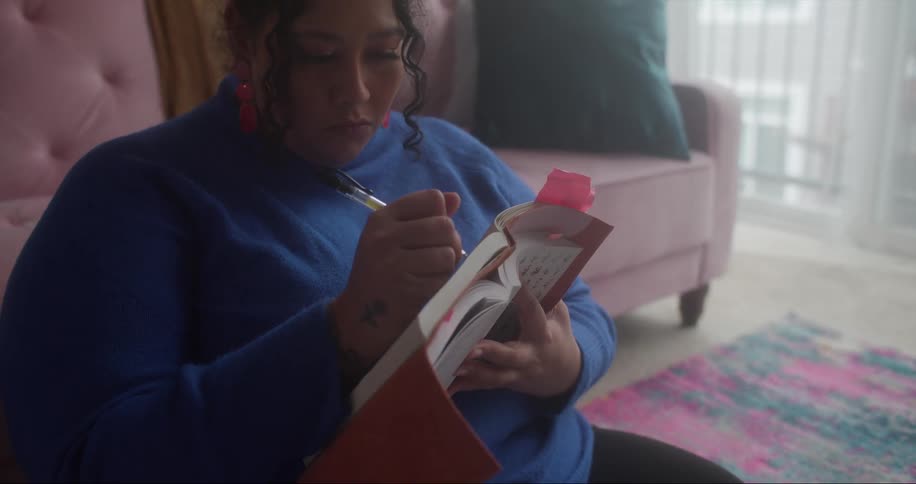 A woman takes notes while reading on the floor of her apartment