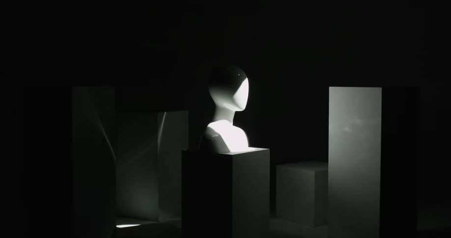 A bright light shines over a dark room where a human bust sits on a pedestal