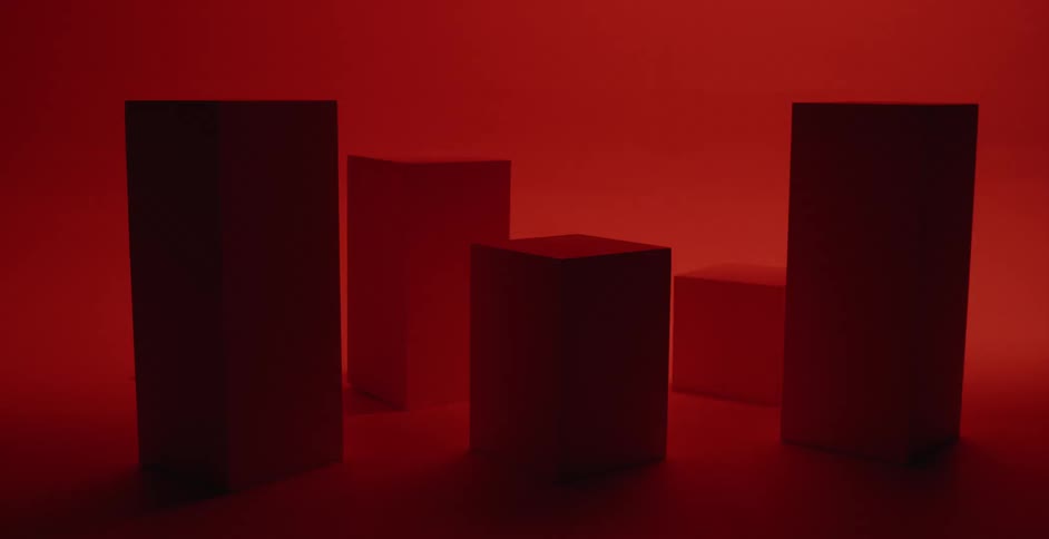 Rectangle shaped boxes are sitting on the floor of an empty room as flashing red lights shine on the boxes and floor as well as the walls