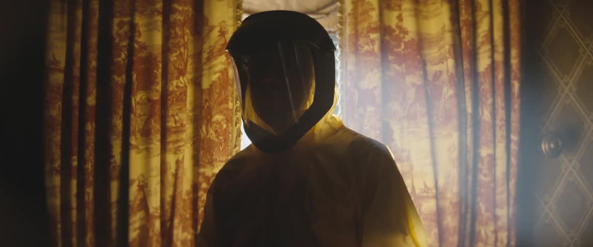 The silhouette of a person completely covered in a yellow plastic hazmat suit while standing inside their home