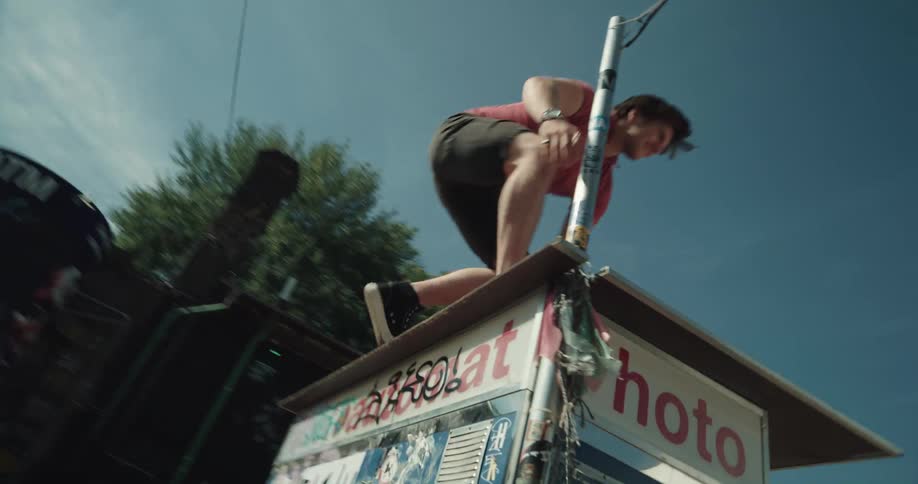 Man climbs onto roof of small graffiti covered stand in town