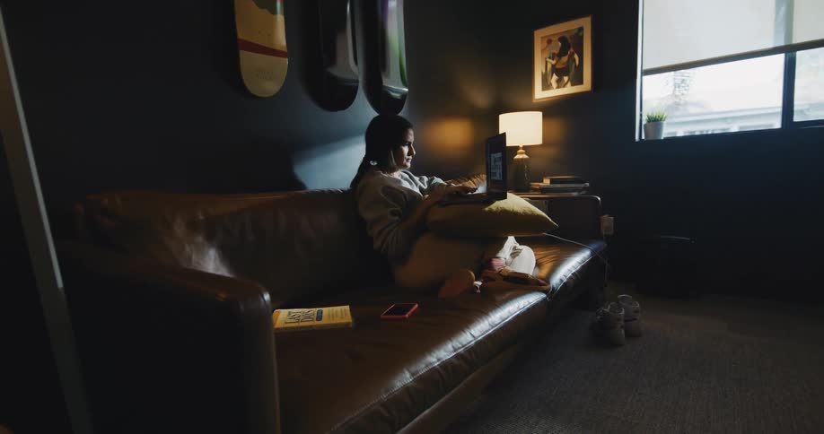 A woman sits on a couch at home and looks at her laptop