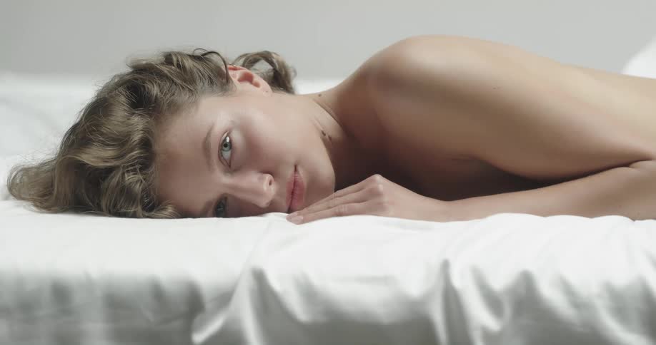 A model opens her eyes while lying face down on white bedding