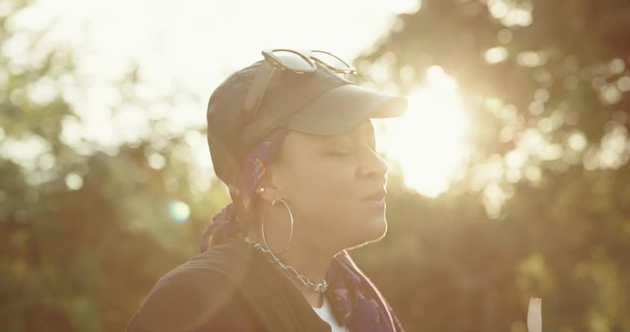 Woman with sunglasses black cap hoopearrings and black jacket have a picnic in picnic area at sunset