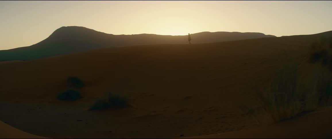 Silhouette of a person standing on top of a hill in the desert as the sun shines brightly on the horizon
