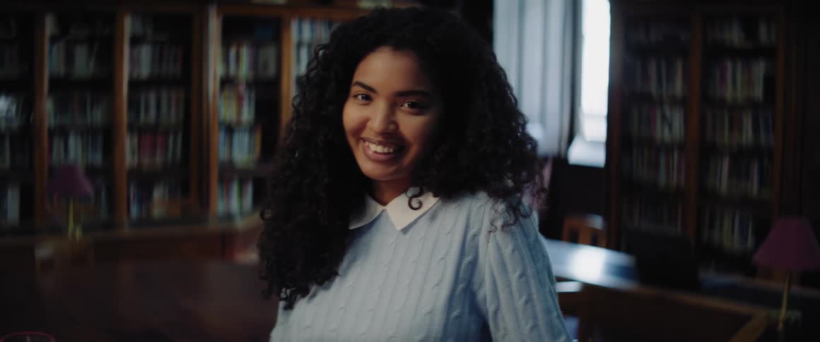 A teenage girl is in a library and she looks up and smiles