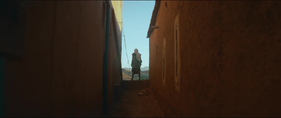A man stands in between two buildings and looks out at the land