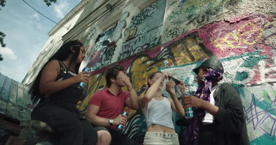 Young adults stand around laughing and dancing as they smoke and drink