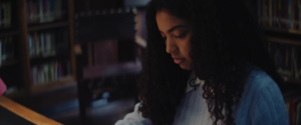 Girl with curly hair and turquois sweater sits at desk writing down in the library
