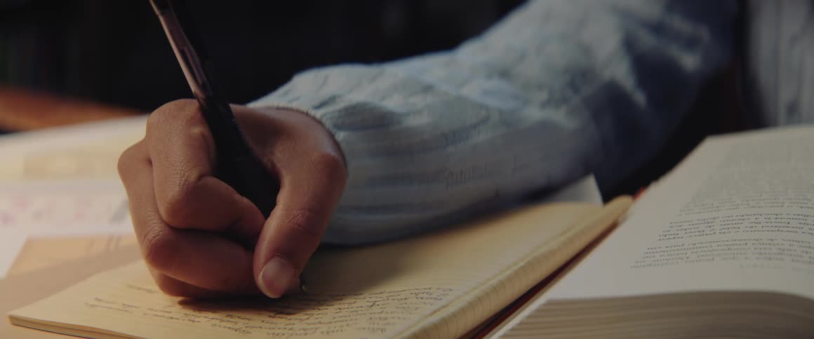Girl with turquoise sweater writes down in notebook sitting at desk in the library
