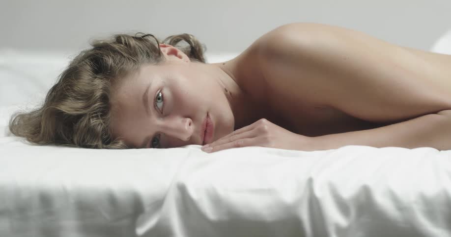 Topless female model with brown wavy hair lies in prone position