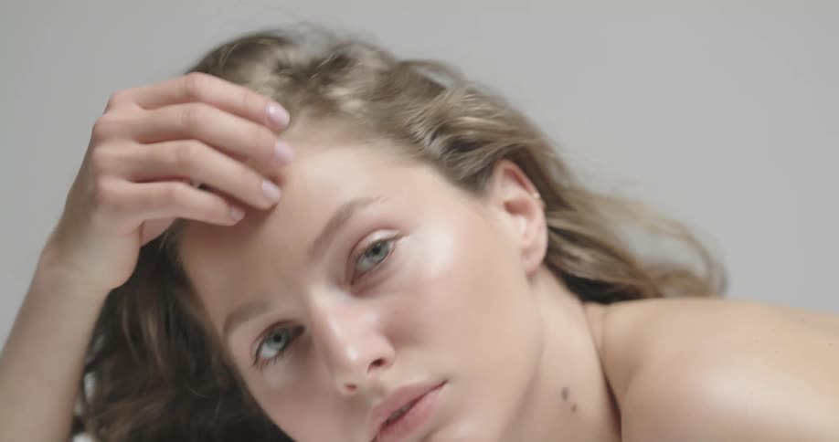 Topless female model with wavy hair lies in prone position looking at camera