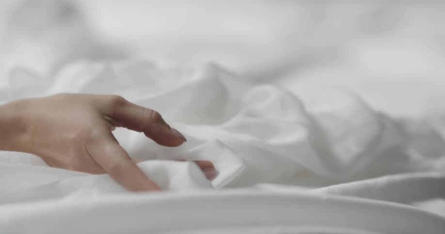 Womans hand with polished fingernails grasps strokes and feels white fabric