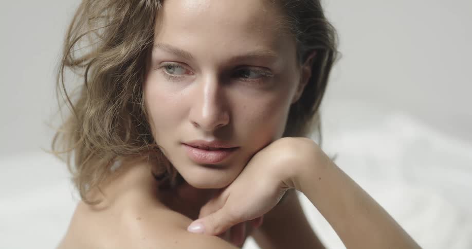 Topless female model with brown wavy hair looks over her shoulder