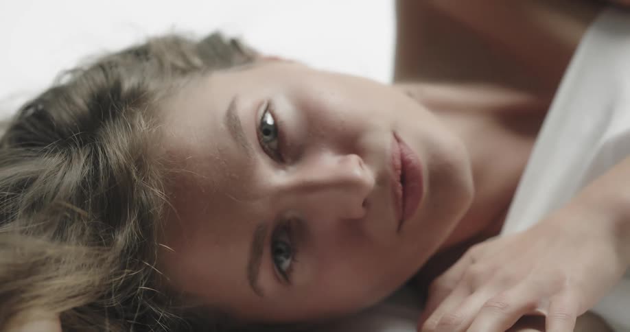 A woman smiles while rolling around under a white bed sheet