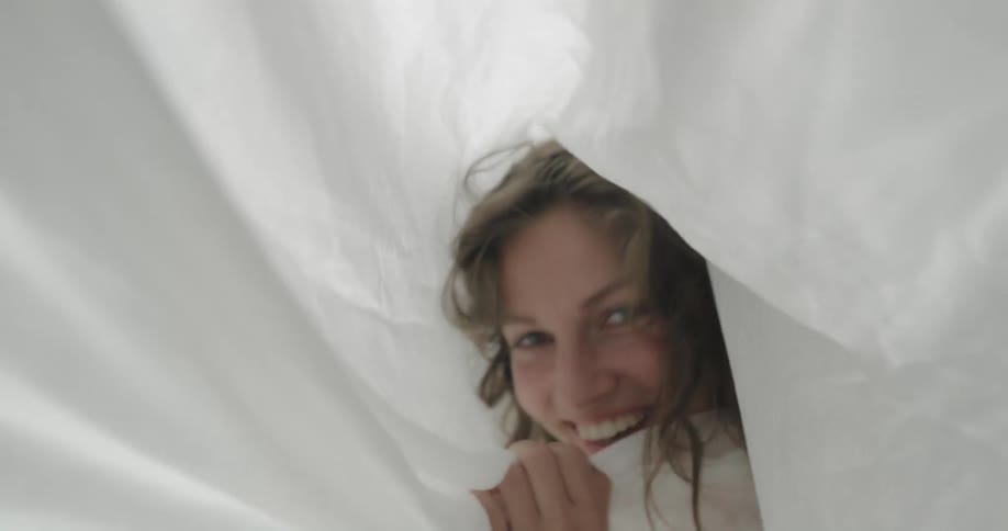 A woman laughs as she hides her face in a white sheet