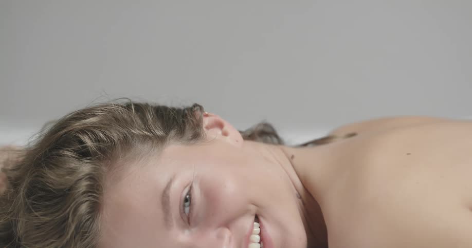 Topless female model lies in prone position laughing