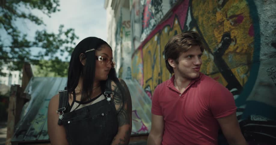 A group of four friends laugh shaking their shoulders near a wall covered in colorful graffiti