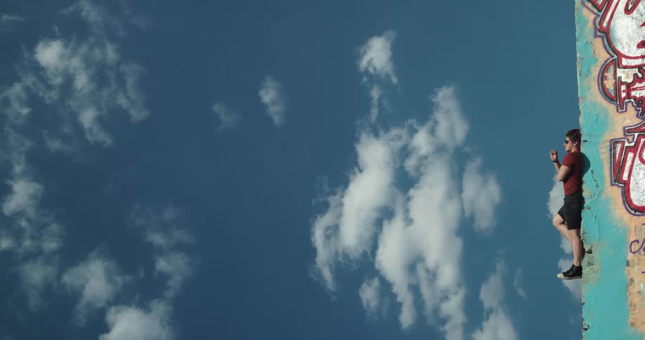 A man lies on a graffitied ledge downtown and looks up at the sky