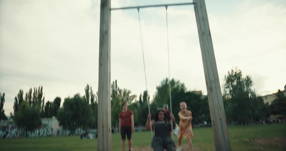 A group is in a park and pushing a teenager on a swing