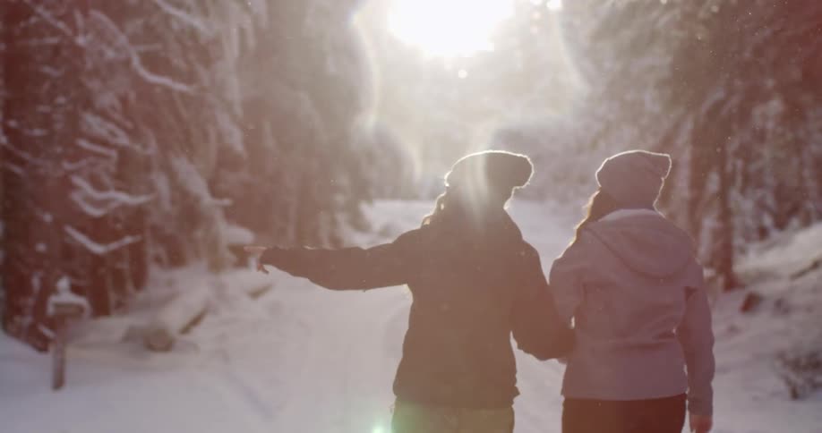 Two women walk down a trail as it snows