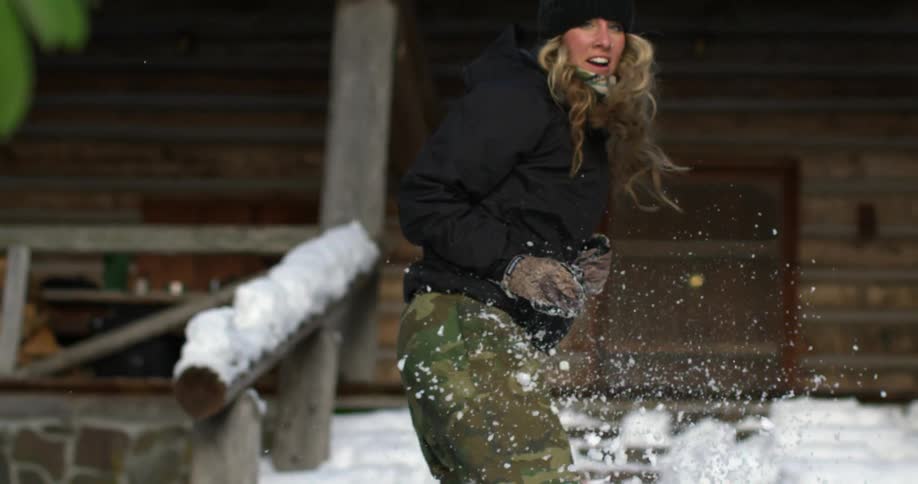 A woman running gets hit with a snowball before turning to grab one herself