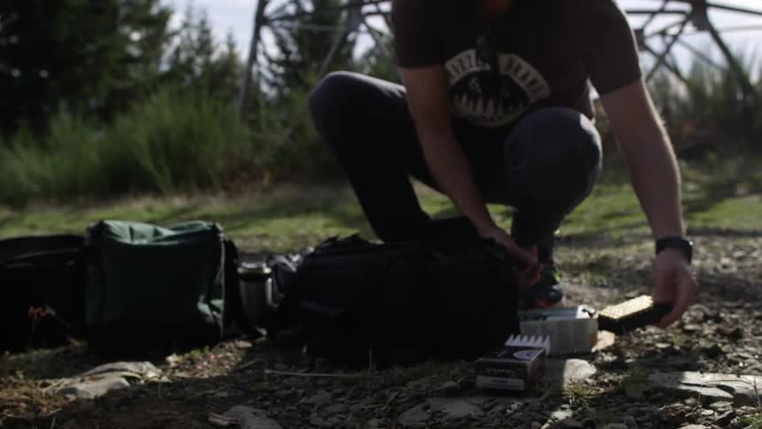 Man crouches and opens a small box in the wilderness
