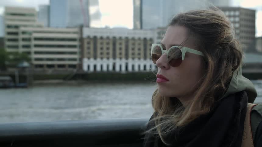 A woman wearing sunglasses is sitting outdoors on a windy day