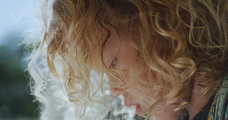 A child with dirty blonde curls outside in the sunshine