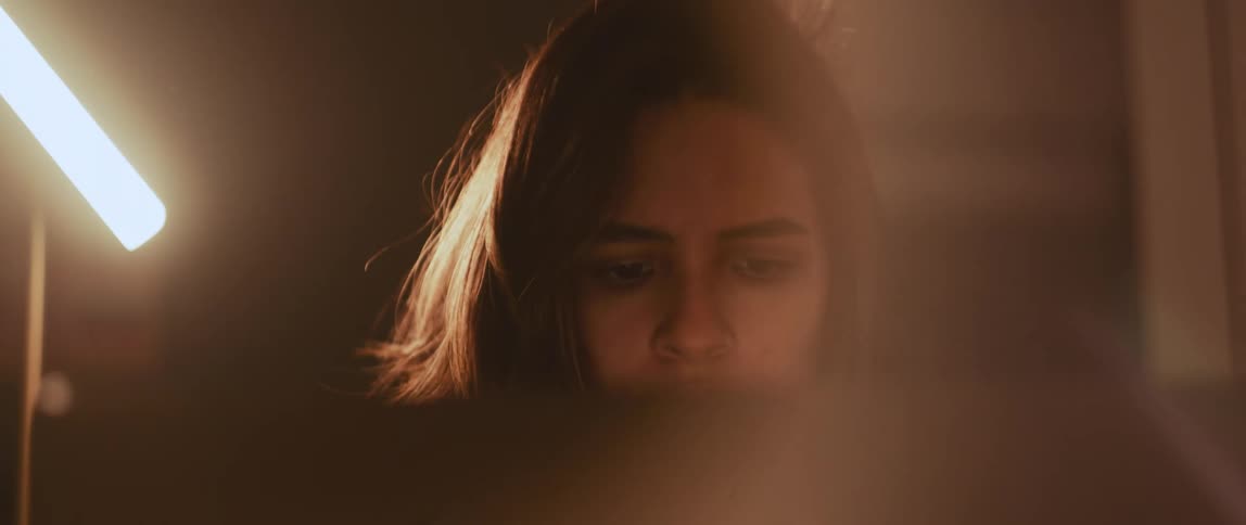 Woman with brown hair sits at desk working on laptop next to table lamp