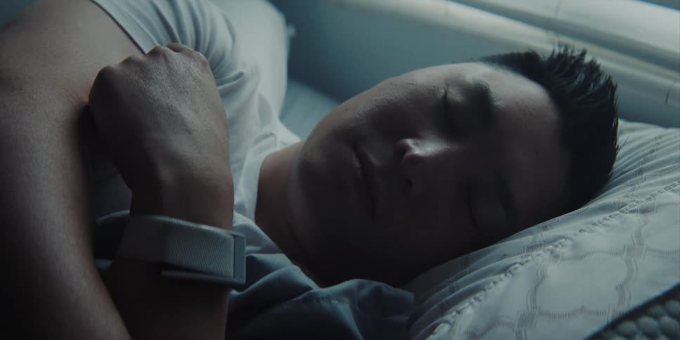 A man asleep on his side on a bed beneath a window