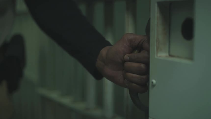 A guard slides a jail cell door closed