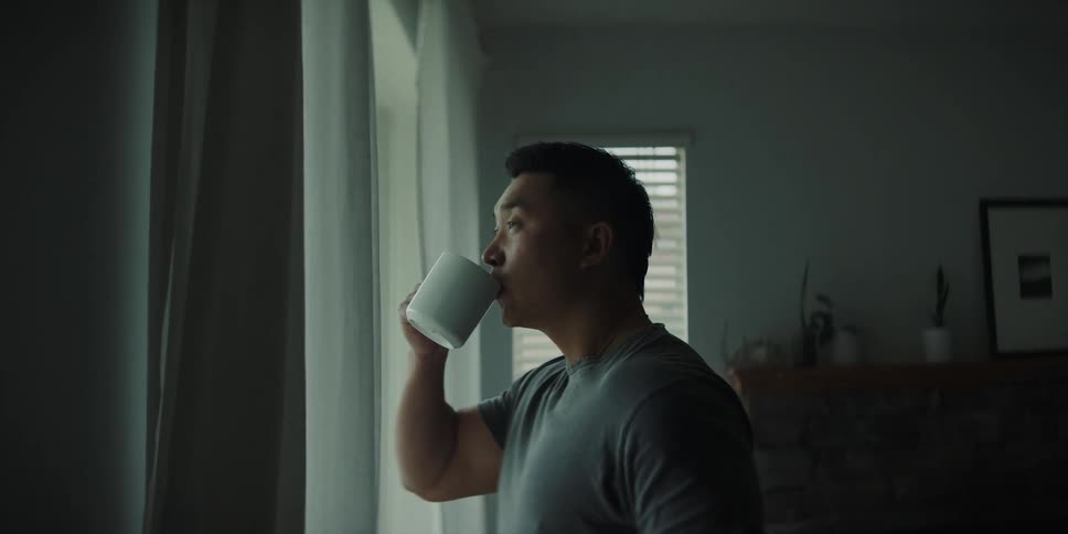 A man drinks coffee while looking out his bedroom window