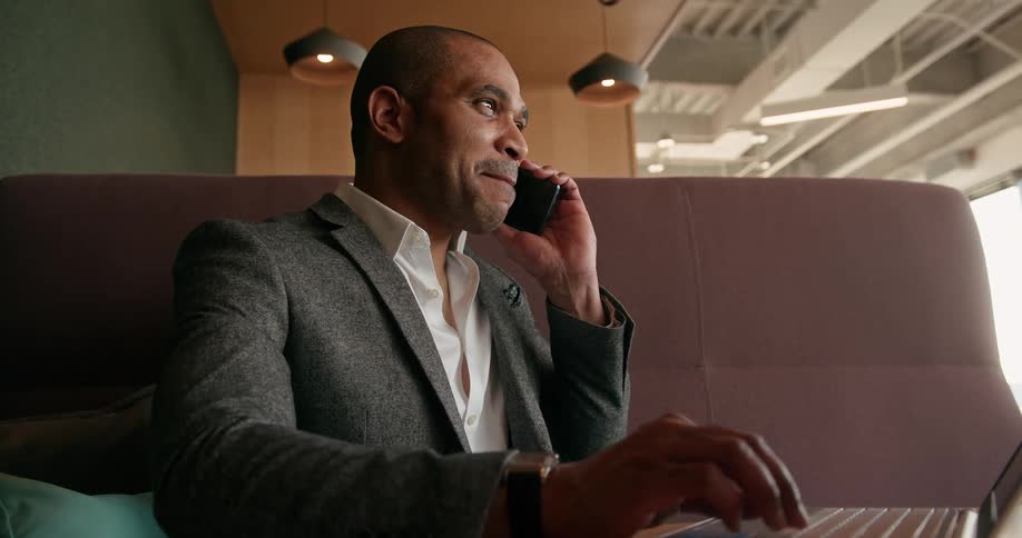 A man is sitting in a building and talking on a phone