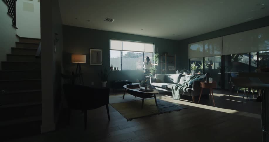 A woman raises the shade on her large living room window letting in the sun
