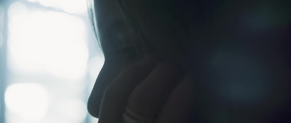 A person is standing quietly in the shadows of a room