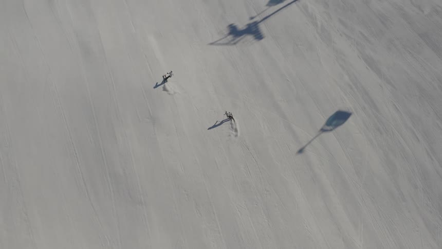 Two skiers moving down the slope cast shadows next to the chair lift on a bright sunny day