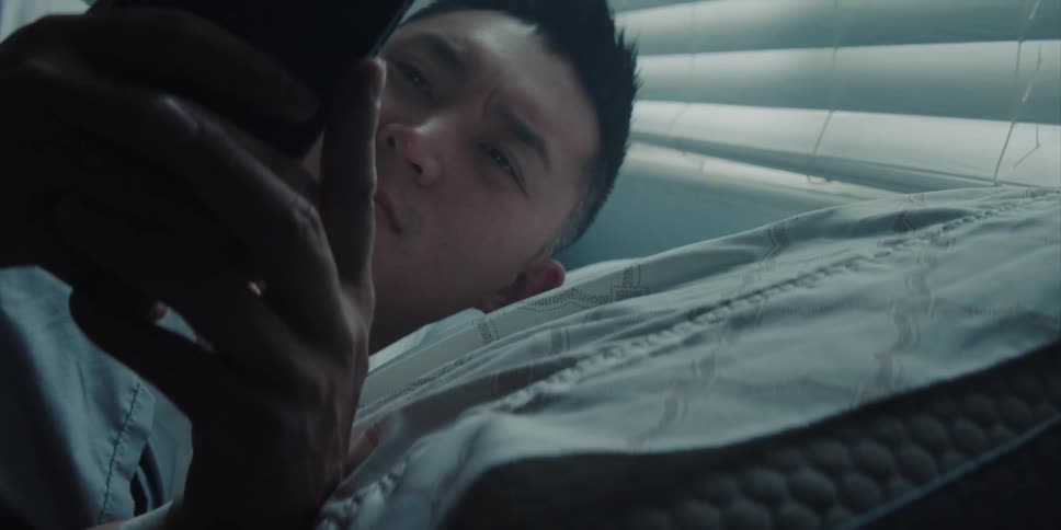 Sleepy man with white shirt wakes up and checks smartphone and goes on to sleep in bed in the morning