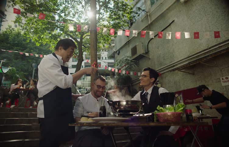 A waiter greets a table of men at an outdoor restaurant full of people