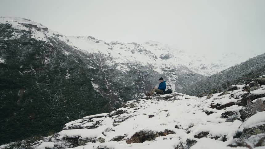 A man sits on the ledge of a mountain