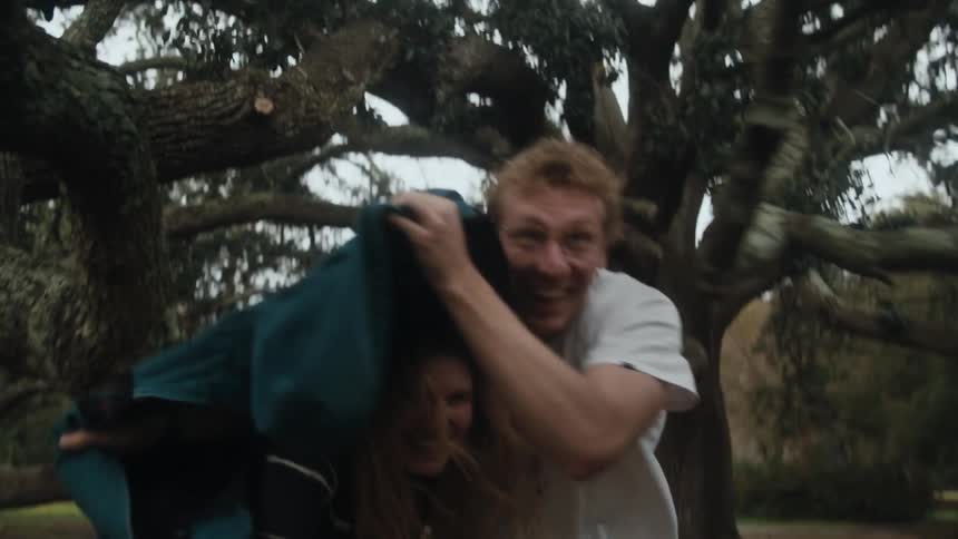 A man and woman caught in a rainshower run and laugh with a coat covering her
