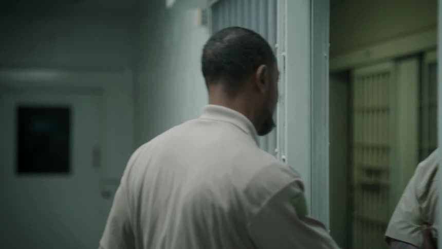A guard leads a prisoner behind bars