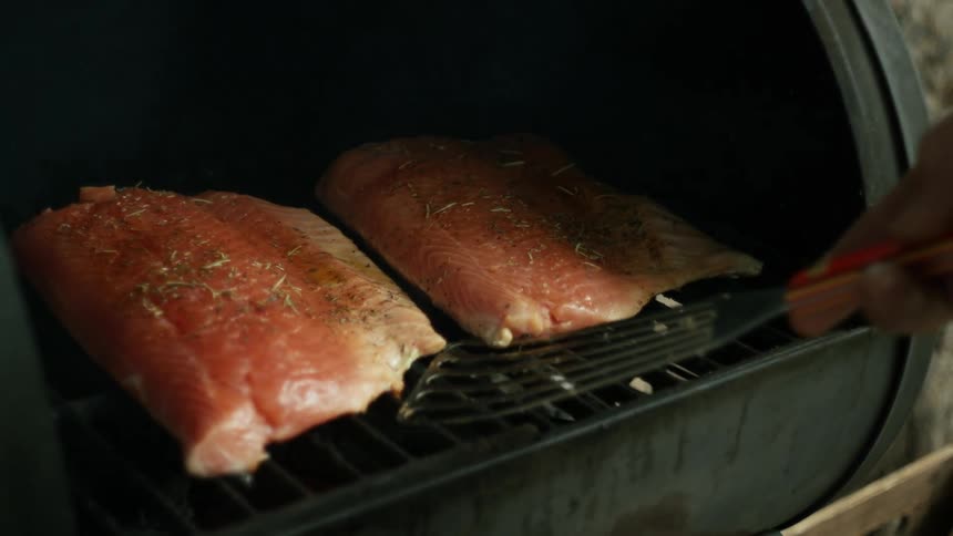 A person is cooking fish outdoors on a grill